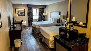 A hotel room with two beds, a desk with a computer, a coffee maker, and a trash bin.