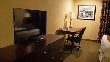 Habitación de hotel con televisión de pantalla plana sobre un tocador, un escritorio con lámpara, una silla y una cama con cortinas.