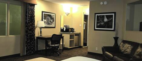 A hotel room with a bed, desk, chair, and a couch.