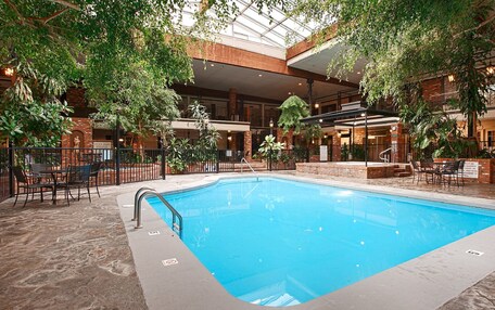 An indoor swimming pool with a glass ceiling, surrounded by indoor seating and greenery.
