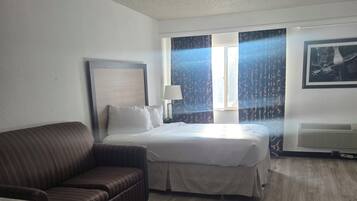 A hotel room with a bed, a sofa, a desk, and a window with curtains.