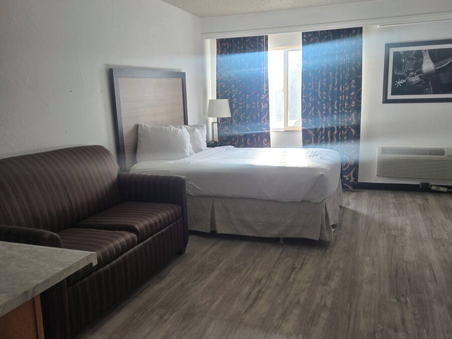 A hotel room with a bed, a sofa, a desk, and a window with curtains.
