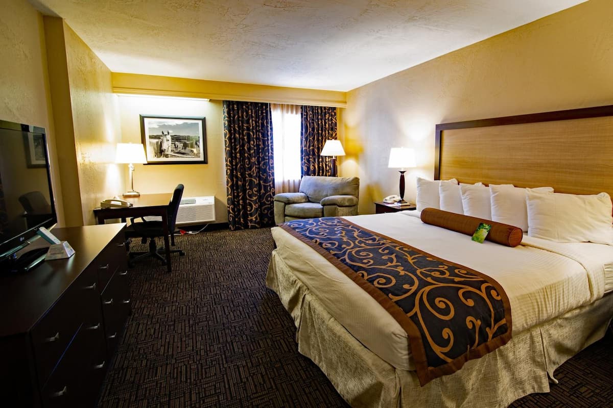 A hotel room with a large bed, a desk with a chair, a television, and a window with curtains.