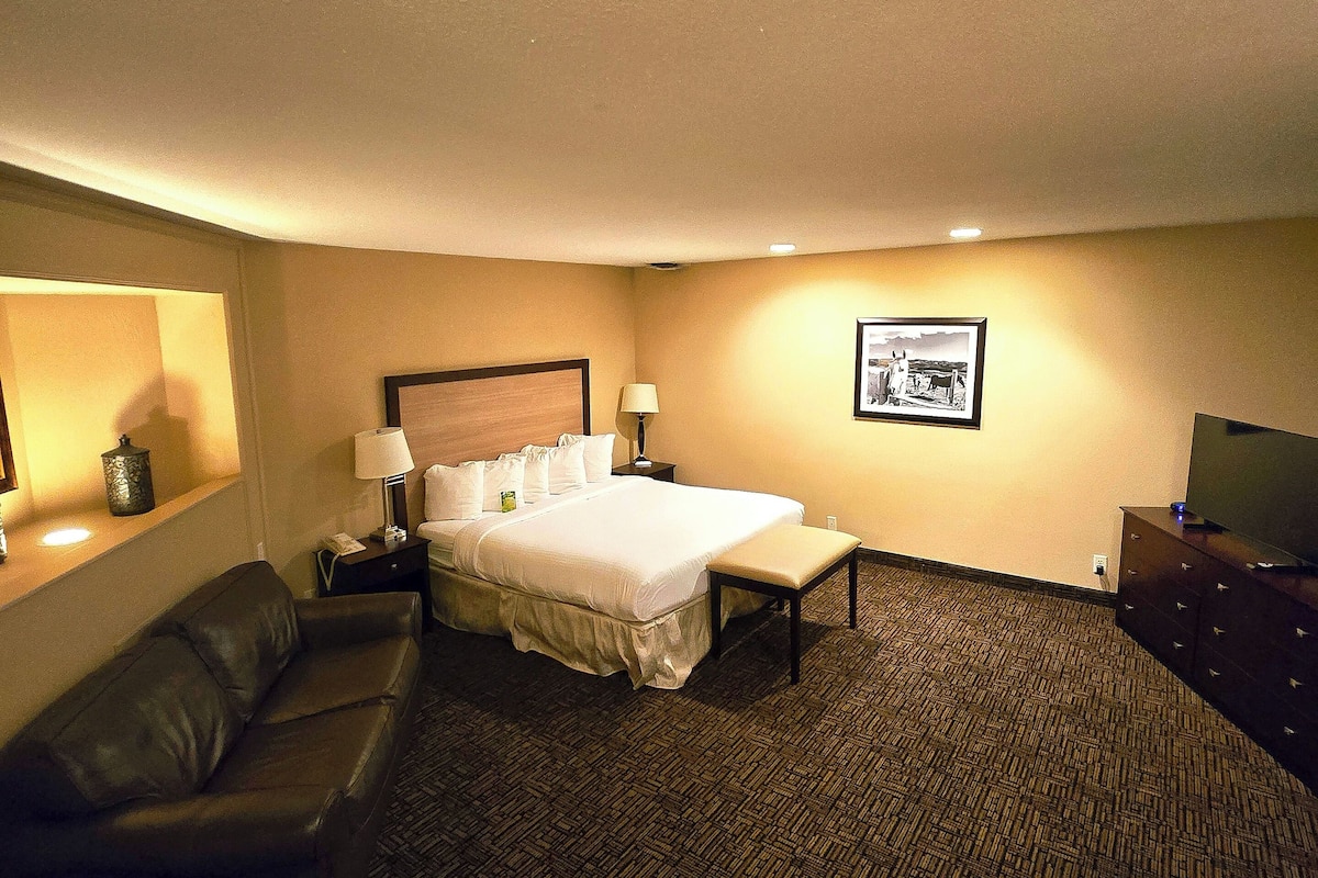 A hotel room with a bed, a desk, a chair, a sofa, and a television.