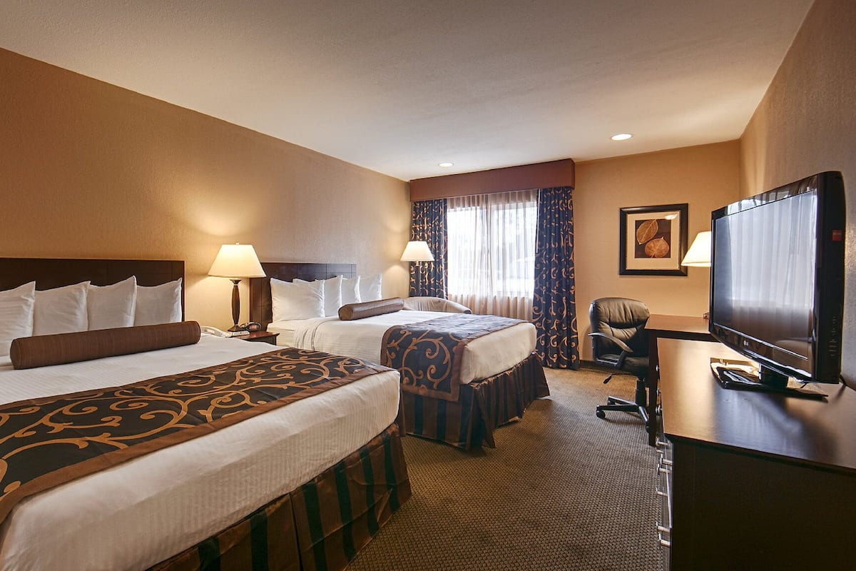 A hotel room with two beds, a desk with a television, and a chair.