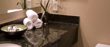 A bathroom with a black marble countertop, white sink, and a toilet. There are framed pictures on the wall and a vase with white flowers on the counter.