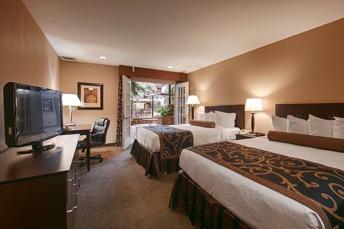 A hotel room with two beds, a desk with a television, and a chair.