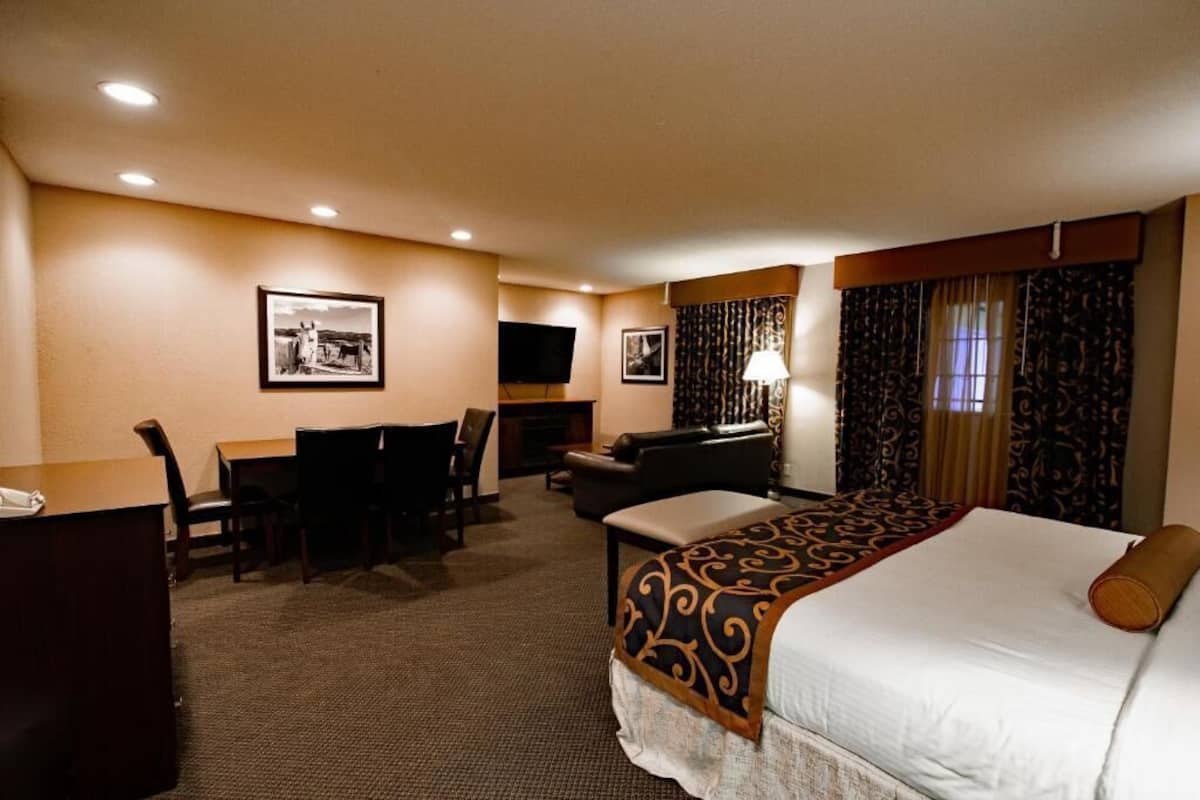 A hotel room with a bed, a desk with a chair, a television, and a fireplace.