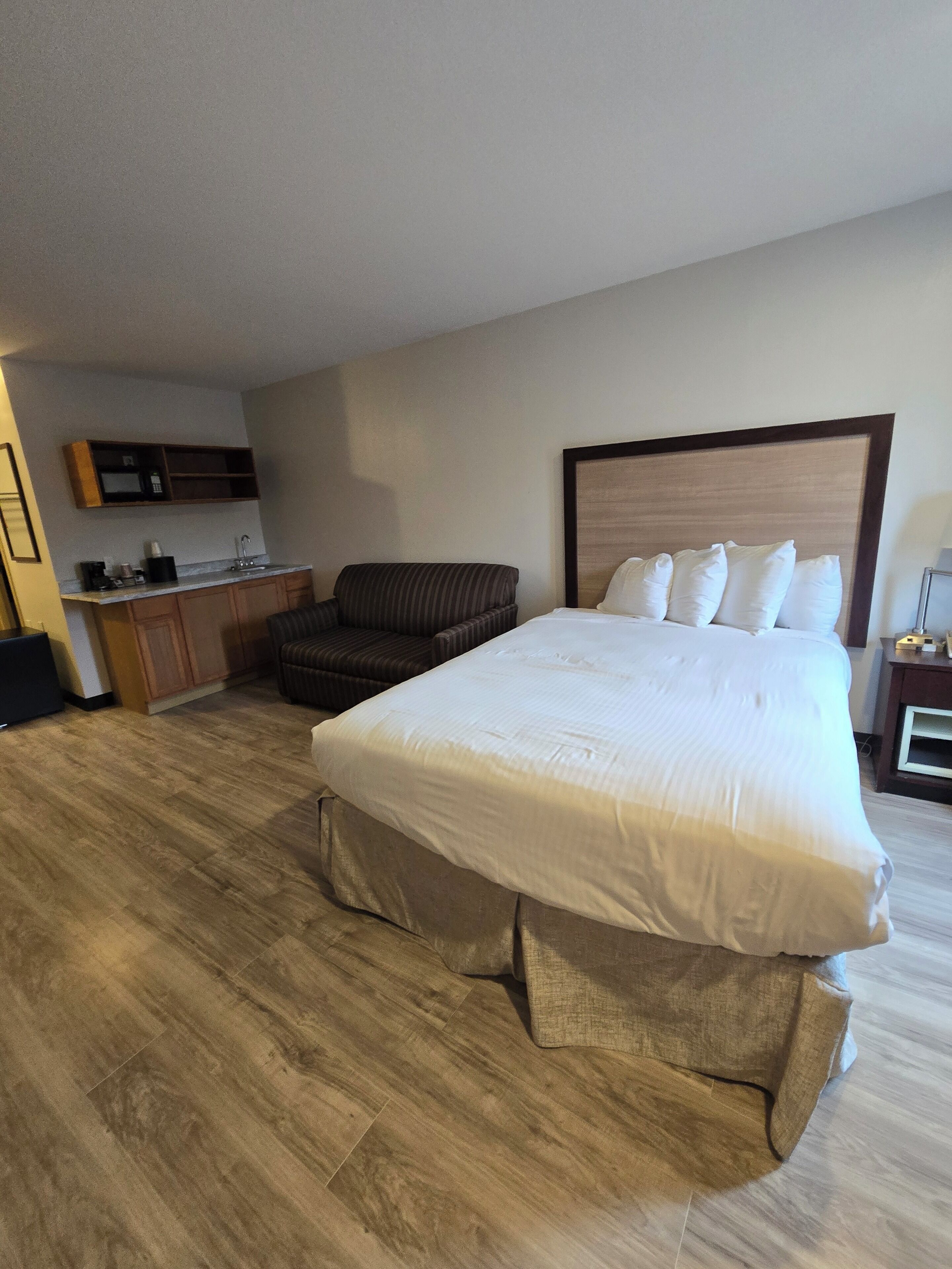 A hotel room with a large bed, a sofa, a kitchenette, and a wooden floor.