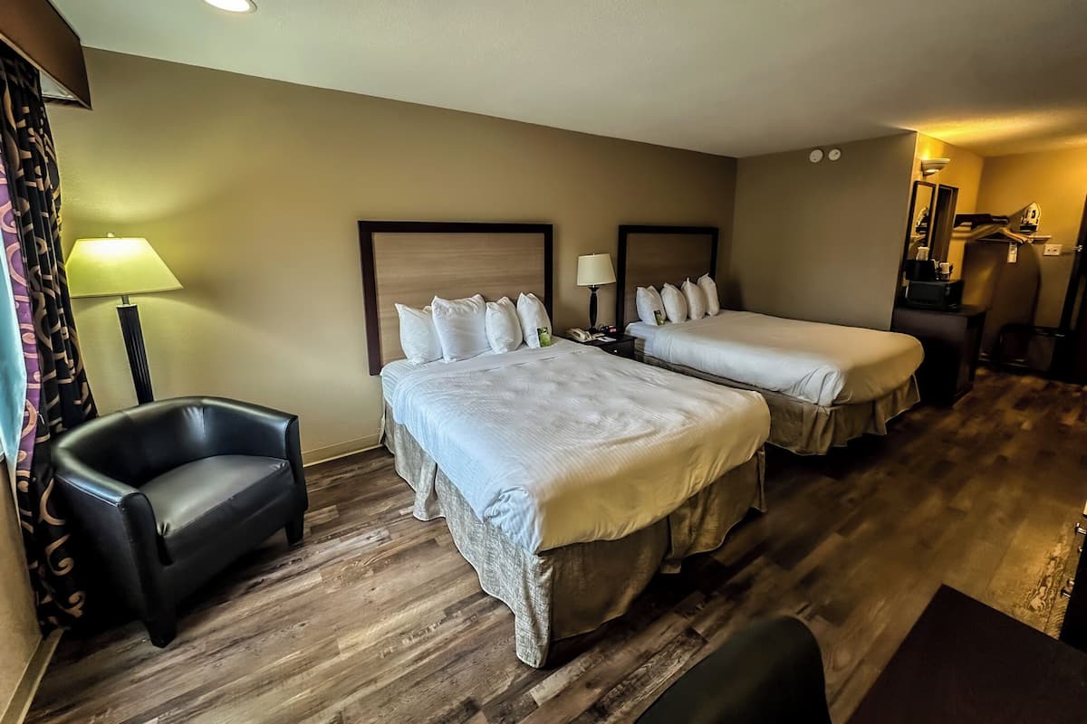 A hotel room with two beds, a chair, a desk, and a mirror.