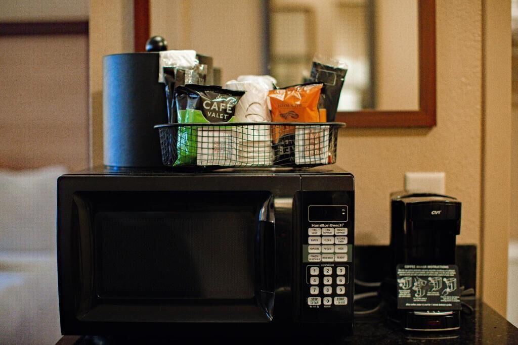 A microwave with a coffee maker and a basket of coffee pods on a countertop.