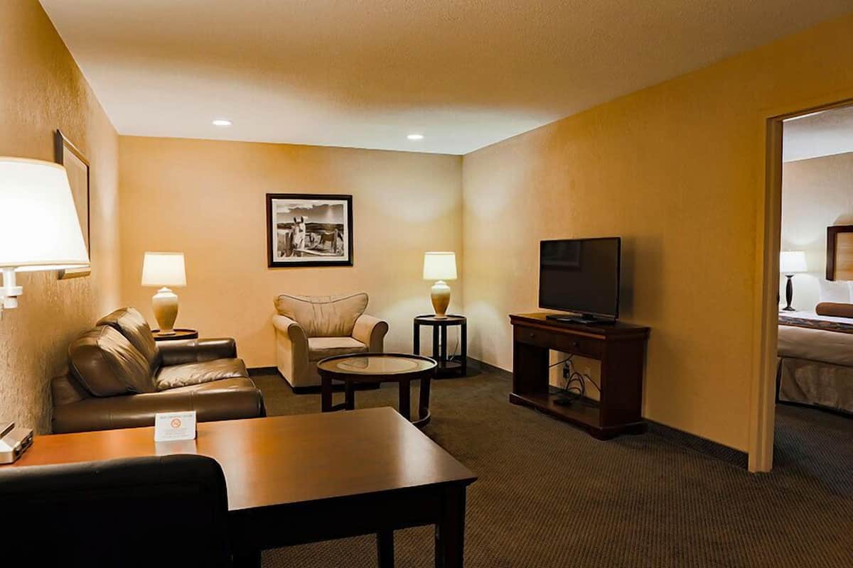 A hotel room with a sofa, armchair, coffee table, TV, and a bed in the background.