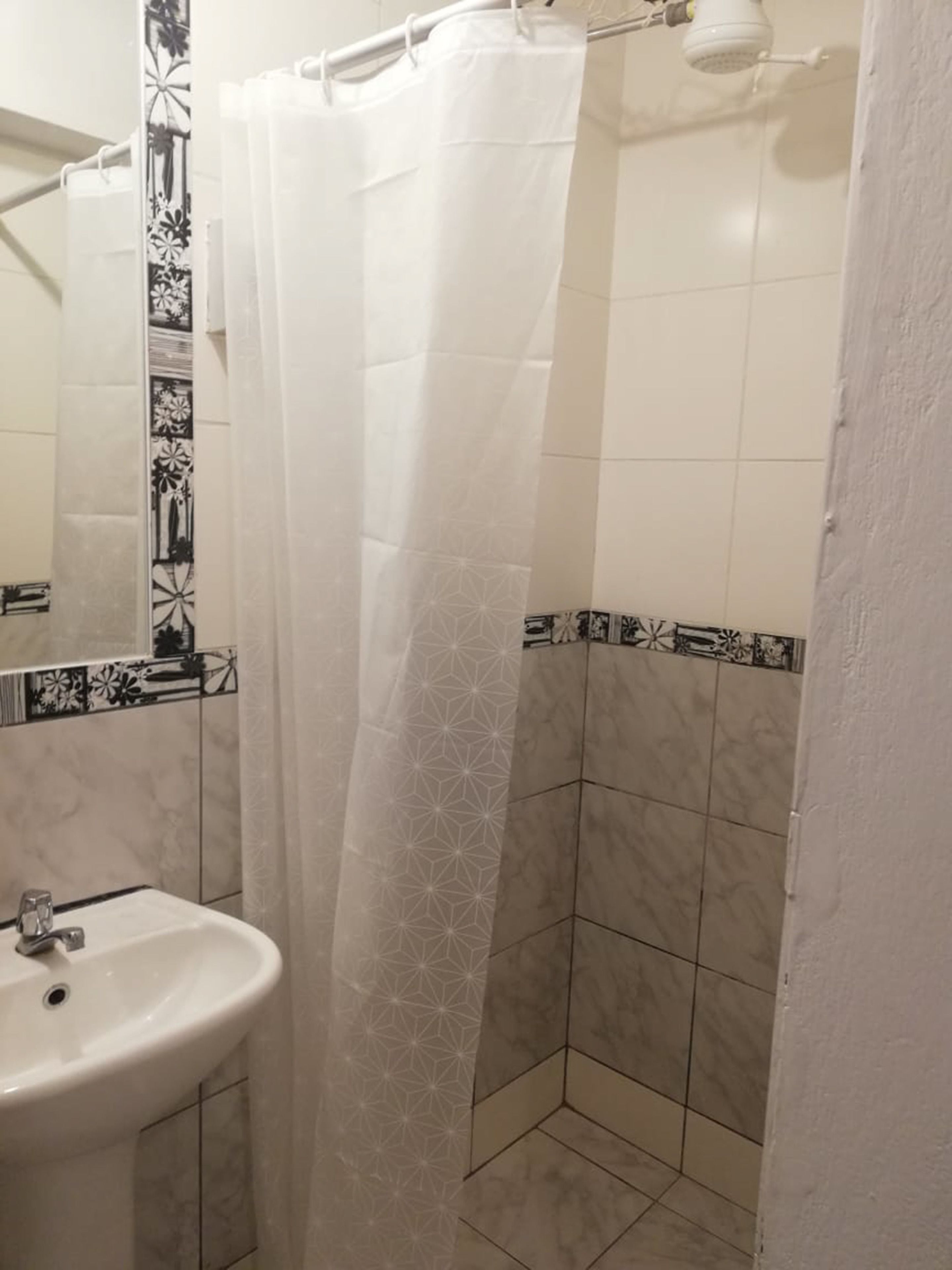 Une salle de bain avec un lavabo blanc, un rideau de douche et des carreaux à motifs.