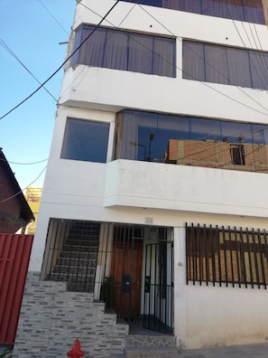 Un edificio de dos pisos con fachada blanca, ventanas grandes y un balcón visible.