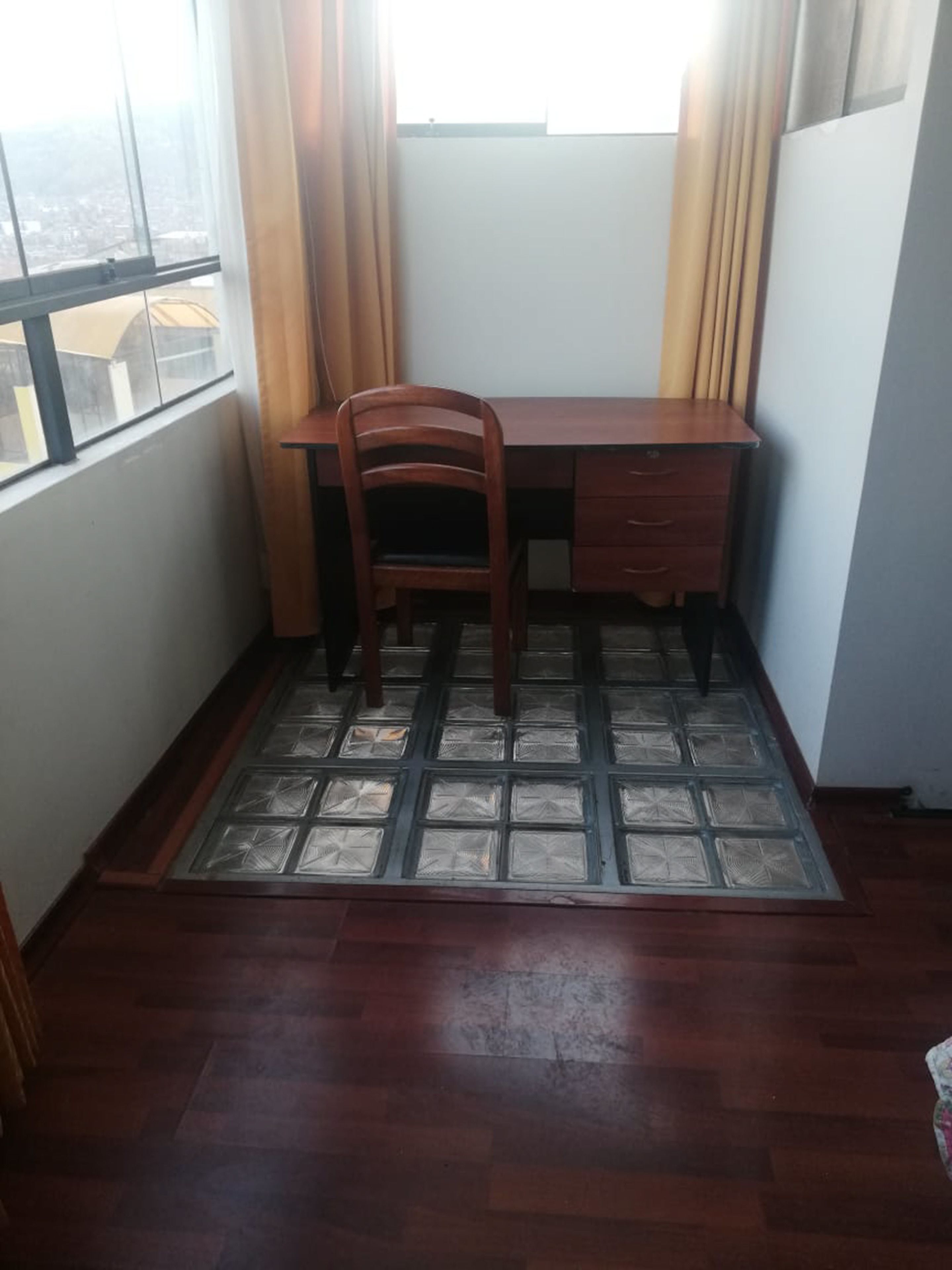 A corner room with a wooden desk, a chair, and a window with curtains.