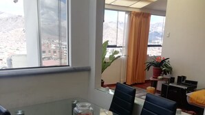 Una zona de menjador moderna amb una taula de vidre, cadires negres i vista a un paisatge urbà a través de grans finestres.