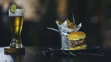 A glass of beer with a lime wedge, a burger, and a small container of fries on a table.