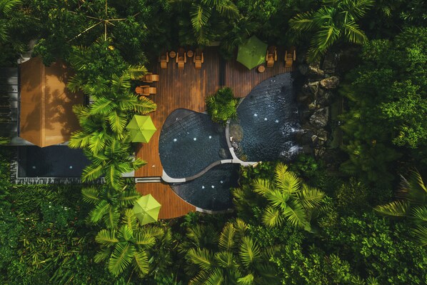 An aerial view of a resort with a wooden deck, outdoor seating, and a water feature surrounded by lush greenery. - Amor Arenal Adults Friendly (La Fortuna)