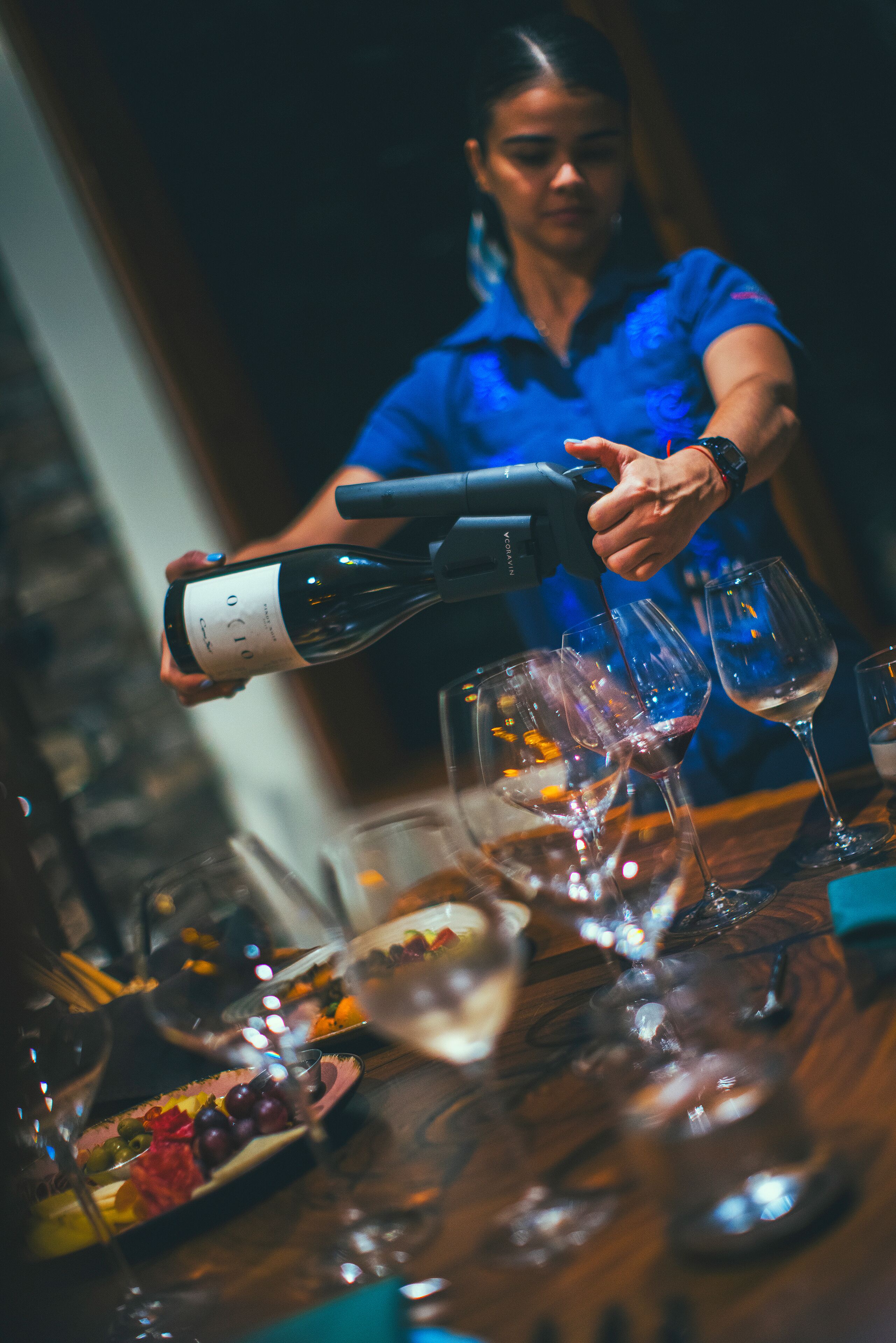 En person hælder vin i glas på et bord med et udvalg af frugter og en vinflaske.