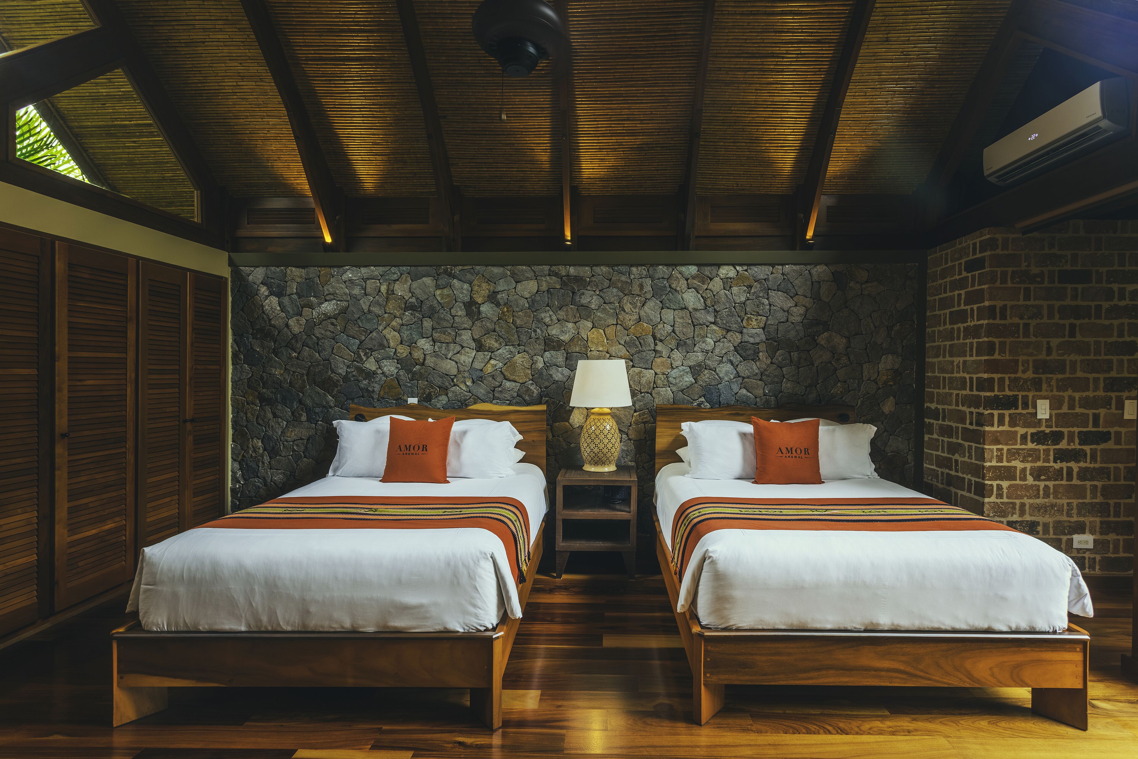 A hotel room with two wooden beds, a stone wall, and a wooden ceiling.
