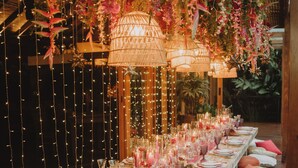 Una larga mesa de comedor preparada para una comida, con luces de cuerda, plantas colgantes y velas.