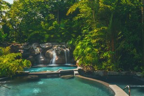 A natural pool with a waterfall surrounded by lush greenery. - Amor Arenal Adults Friendly (La Fortuna)