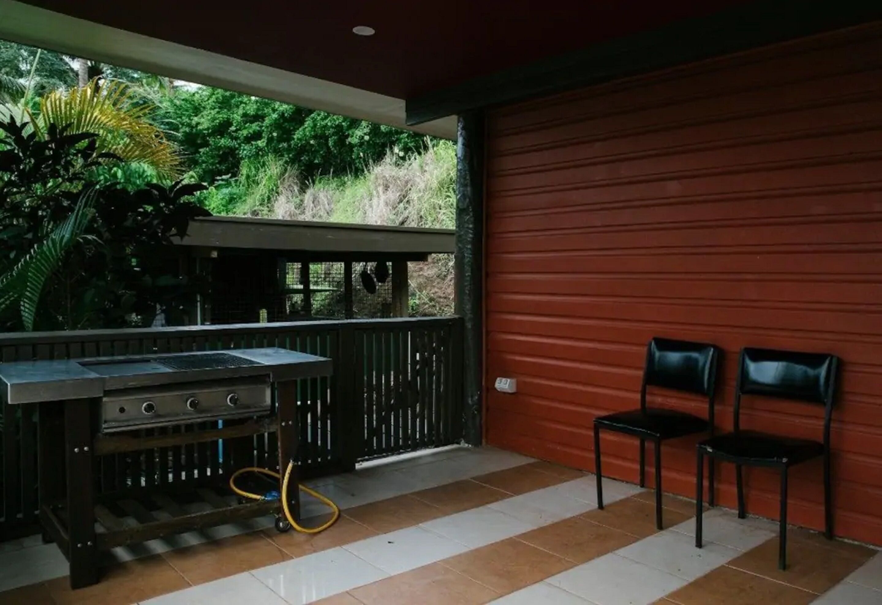 Une terrasse extérieure avec un barbecue, deux chaises et une porte de garage rouge.