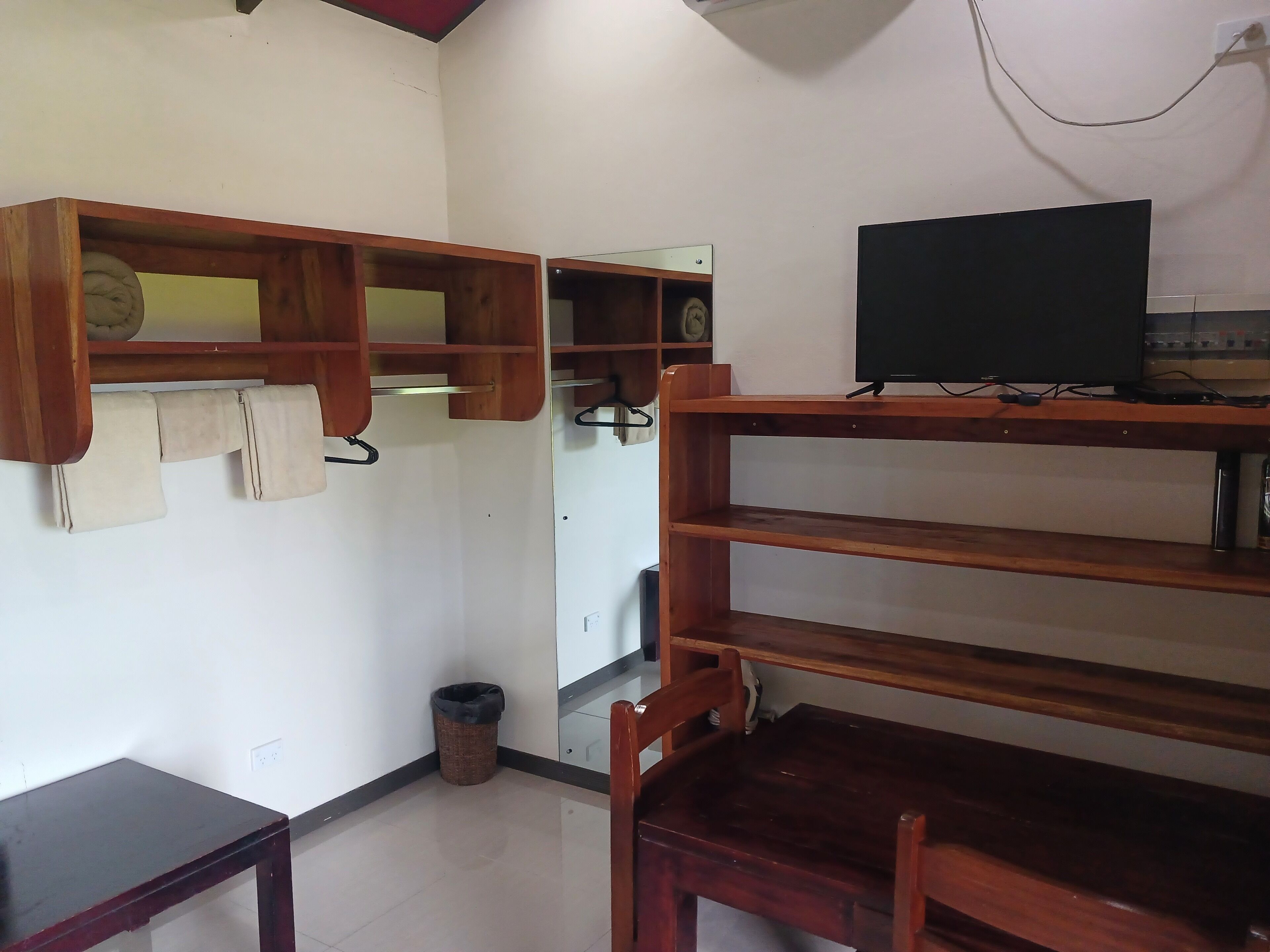 A room with wooden shelves, a television, a small table, and a trash bin.