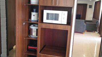 A kitchen with a built-in microwave, a coffee maker, and a rice cooker on open shelves.