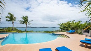 A swimming pool with blue lounge chairs and palm trees, overlooking a body of water. - Dreamview Villas - In Rakiraki (Rakiraki)