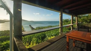 A wooden deck with a table and chairs overlooking a coastal landscape with greenery and a view of the sea. - Dreamview Villas - In Rakiraki (Rakiraki)