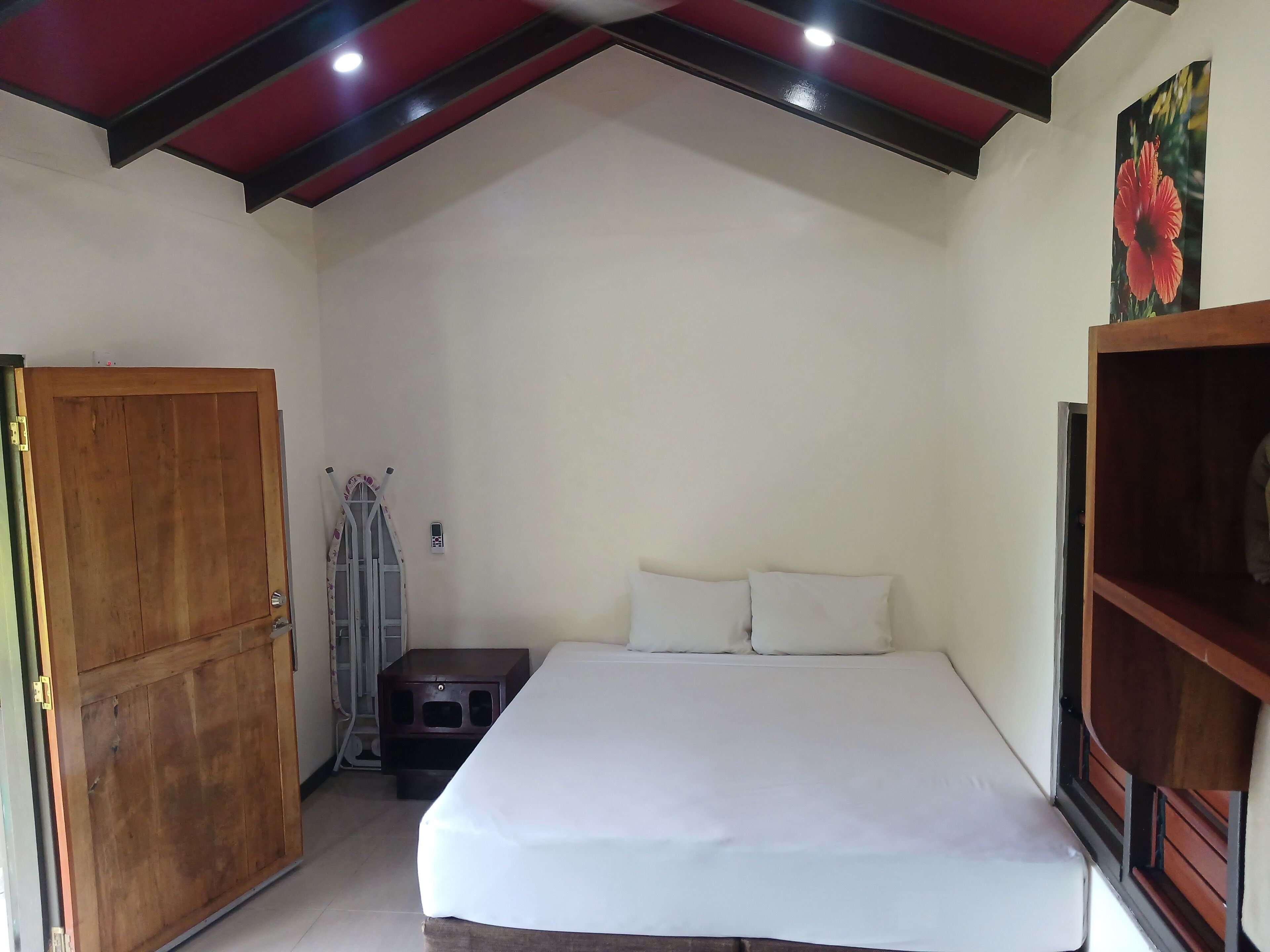 Une chambre à coucher comprenant un lit, une armoire en bois, un petit tabouret et une étagère fixée au mur.