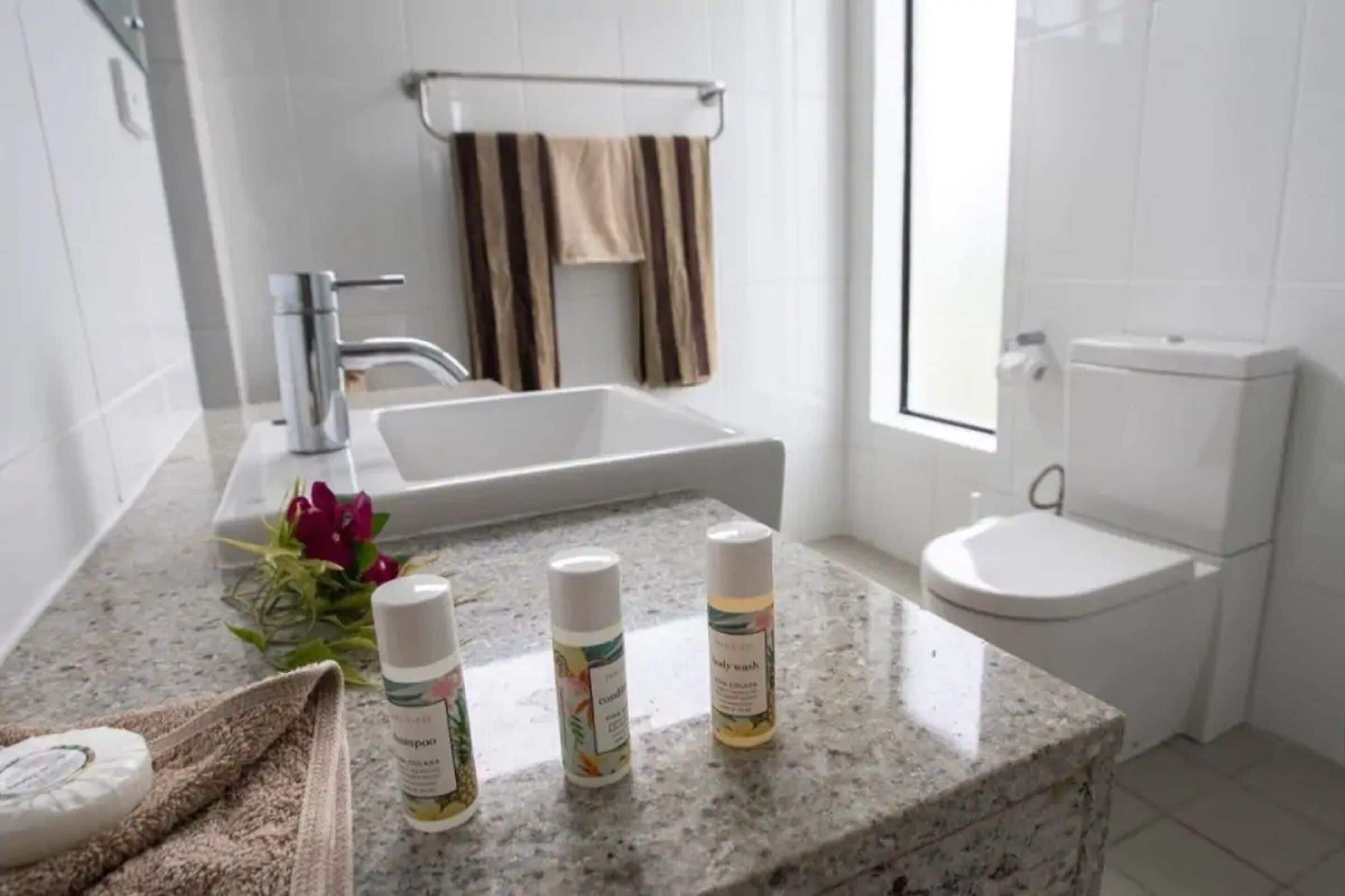 A bathroom with a granite countertop, a white sink, a toilet, and a towel rack with striped towels.