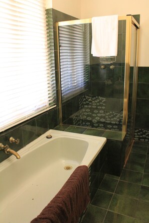 A bathroom with a bathtub, a shower, and a window with blinds. - Cockburn House (Jamestown)