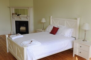 A neatly made bed with white linens and a red pillow, a white nightstand with a lamp, and a fireplace with a 'LOVE' sign above it. - Cockburn House (Jamestown)