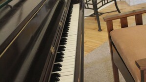 Huoneessa on piano, takka, pöytä ja maljakko, jossa on kukkia.