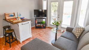 Un espacio habitable compacto con kitchenette, sofá, televisor y una pequeña mesa de comedor.