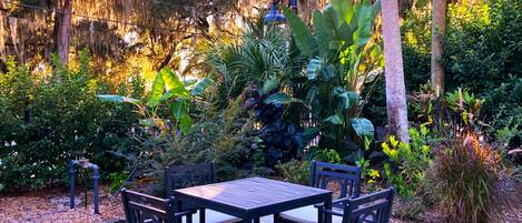 An outdoor patio with a table and chairs, surrounded by lush greenery and trees with Spanish moss.