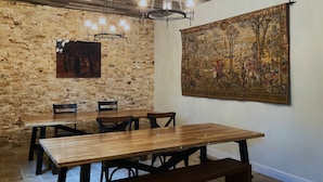 A dining area with a rustic brick wall, a wooden table with benches, and a large tapestry on the wall.