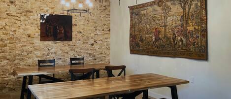 A dining area with a rustic brick wall, a wooden table with benches, and a large tapestry on the wall.