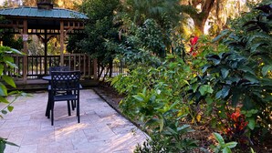 A gazebo with a tiled patio, surrounded by lush greenery and a wooden fence.