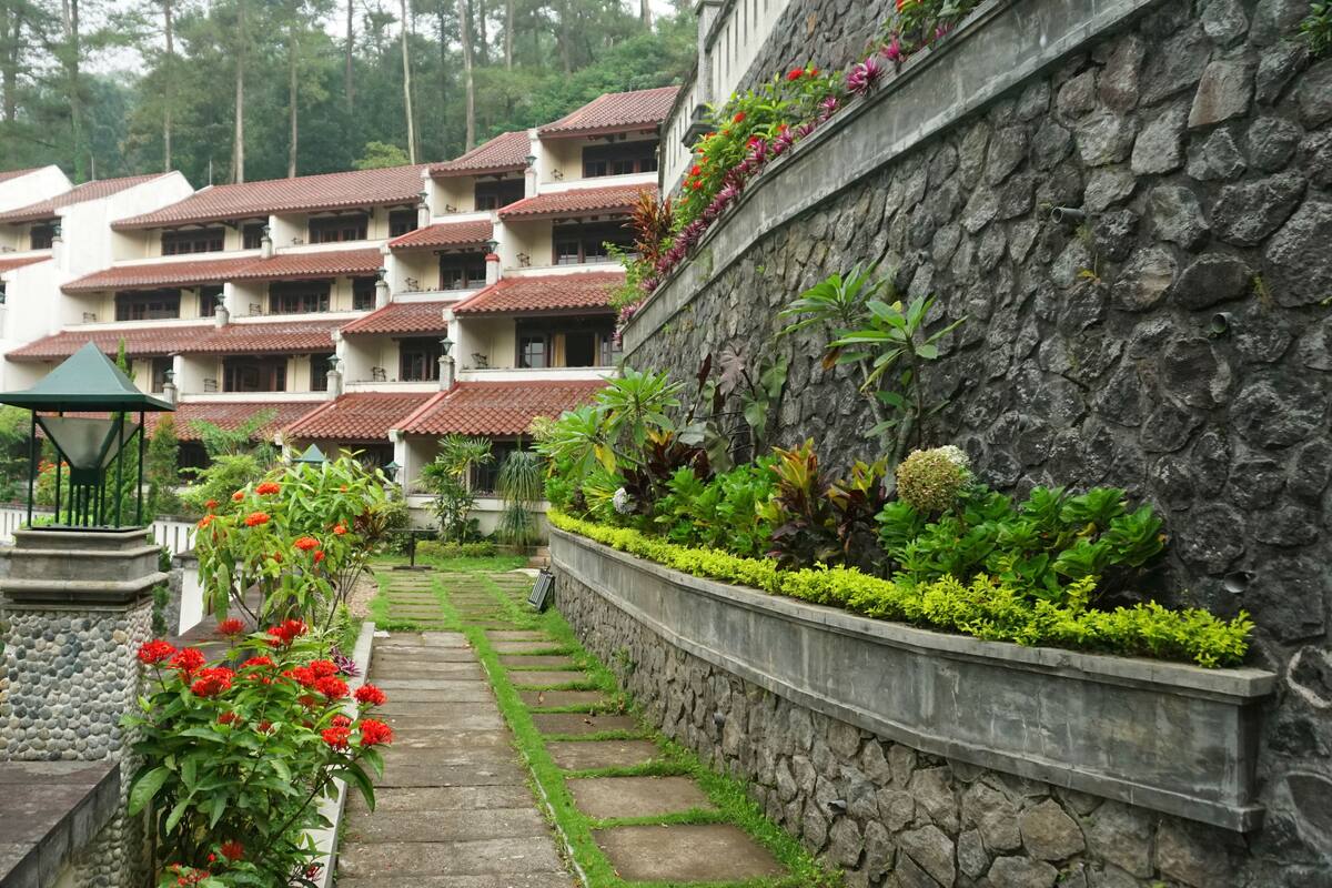 Un hotel con diversi edifici bianchi e tetti rossi, un muro in pietra con vegetazione e un vialetto che conduce all'ingresso.