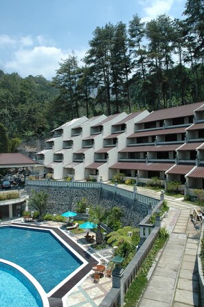 A hotel with multiple floors, a swimming pool, and a mountainous backdrop. - Pines Garden Resort (Prigen)