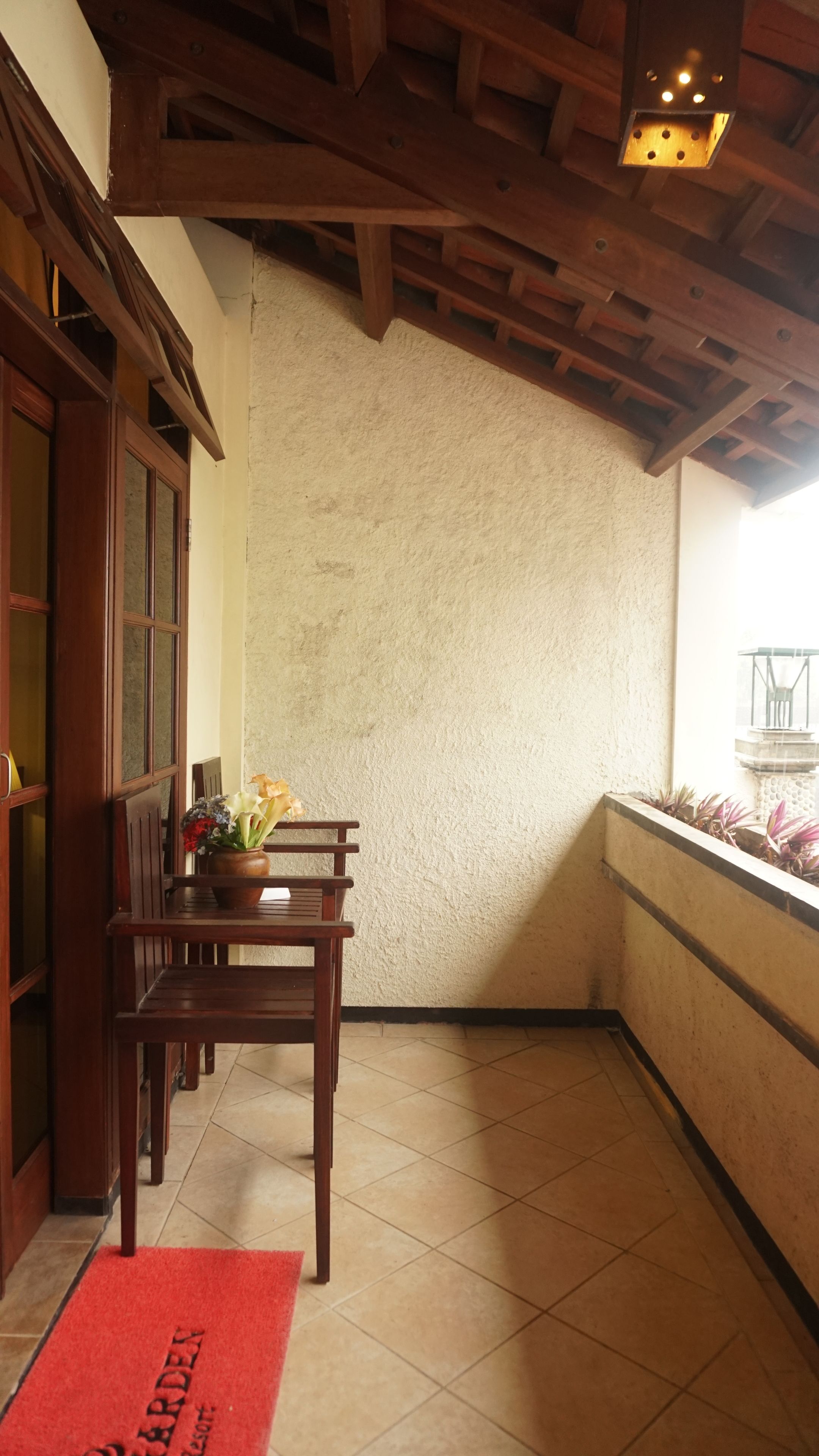 A corner of a room with a wooden bench, a red doormat, and a view of a garden through a window.