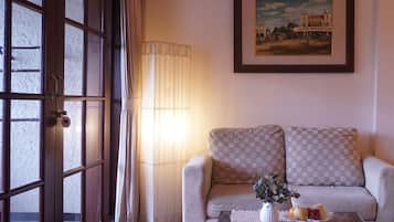A living room with a sofa, a table with a vase and fruit, a lamp, and a painting on the wall.