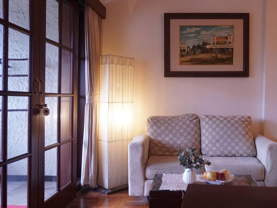 A living room with a sofa, a table with a vase and fruit, a lamp, and a painting on the wall.