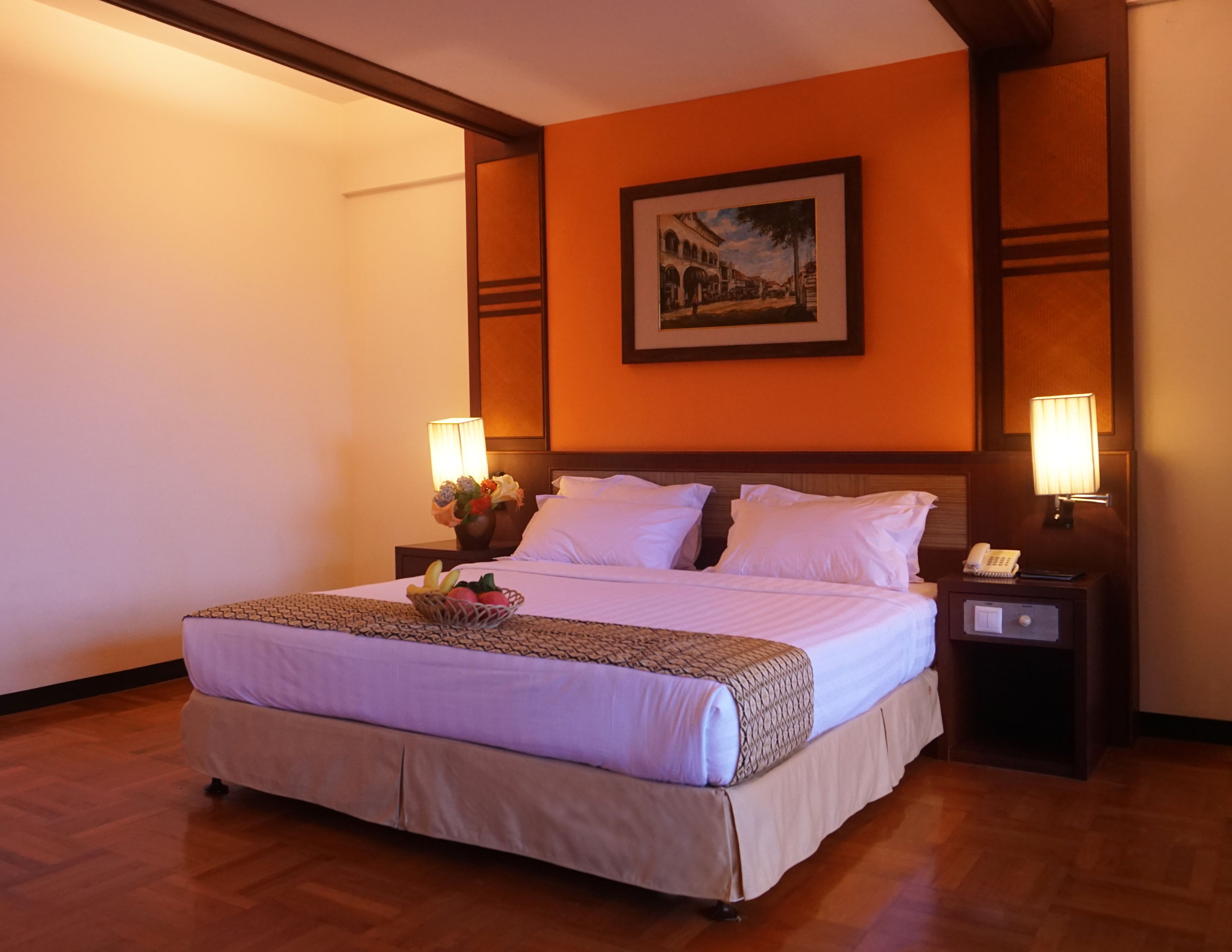 Habitación de hotel con una cama grande, dos lámparas de noche, una mesita de noche con un teléfono y un cuadro en la pared.