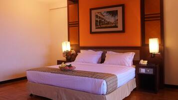 Habitación de hotel con una cama grande, dos lámparas de noche, una mesita de noche con un teléfono y un cuadro en la pared.