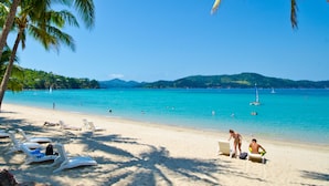 Une plage avec des chaises longues blanches, un rivage sablonneux et une mer d’un bleu limpide.