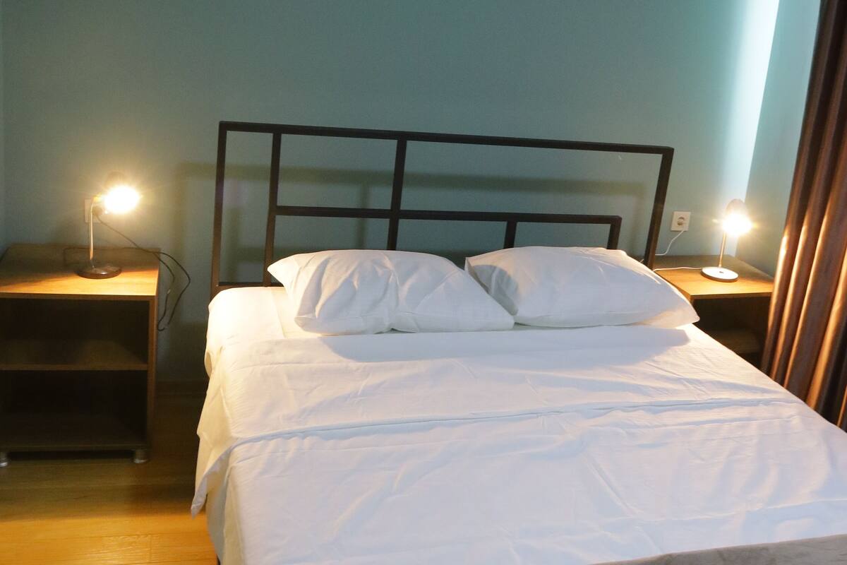 Una cama bien hecha con sábanas blancas en una habitación con paredes verde azulado y suelo de madera.